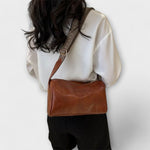 Brown leather-look crossbody bag with woven strap on shoulder, flap-style top.