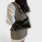 Black crossbody bag with woven strap over shoulder, compact rectangular silhouette.