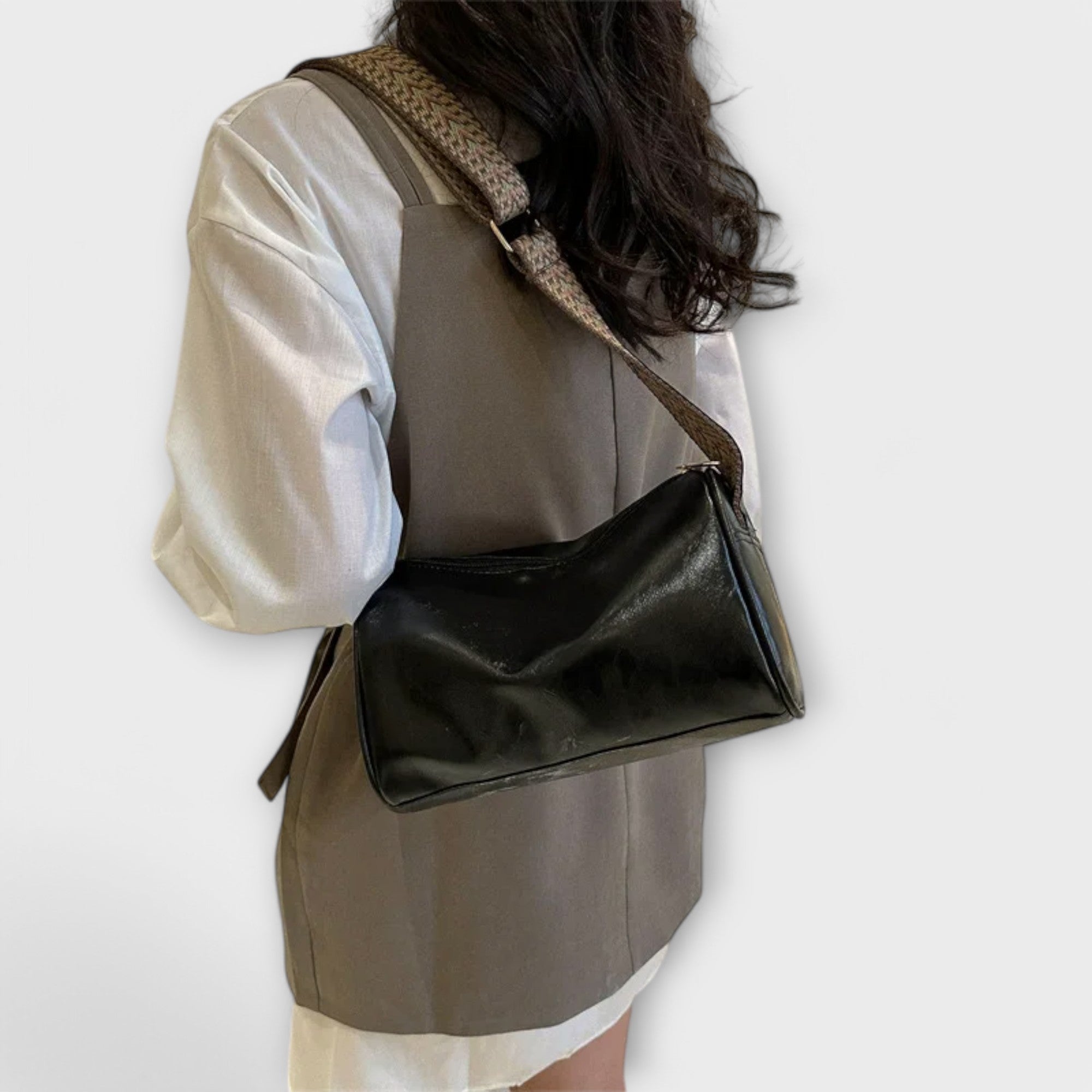 Black crossbody bag with woven strap over shoulder, compact rectangular silhouette.