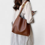 Brown shoulder bag worn on side with gold buckle strap.
