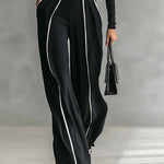Black wide-leg jumpsuit with high neck, belt buckle, and contrast vertical piping