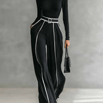 Black high-neck wide-leg jumpsuit with long sleeves, vertical piping, and belt buckle