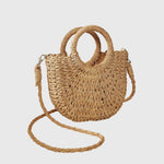Khaki-beige woven straw shoulder bag with ring handles and long braided crossbody strap.