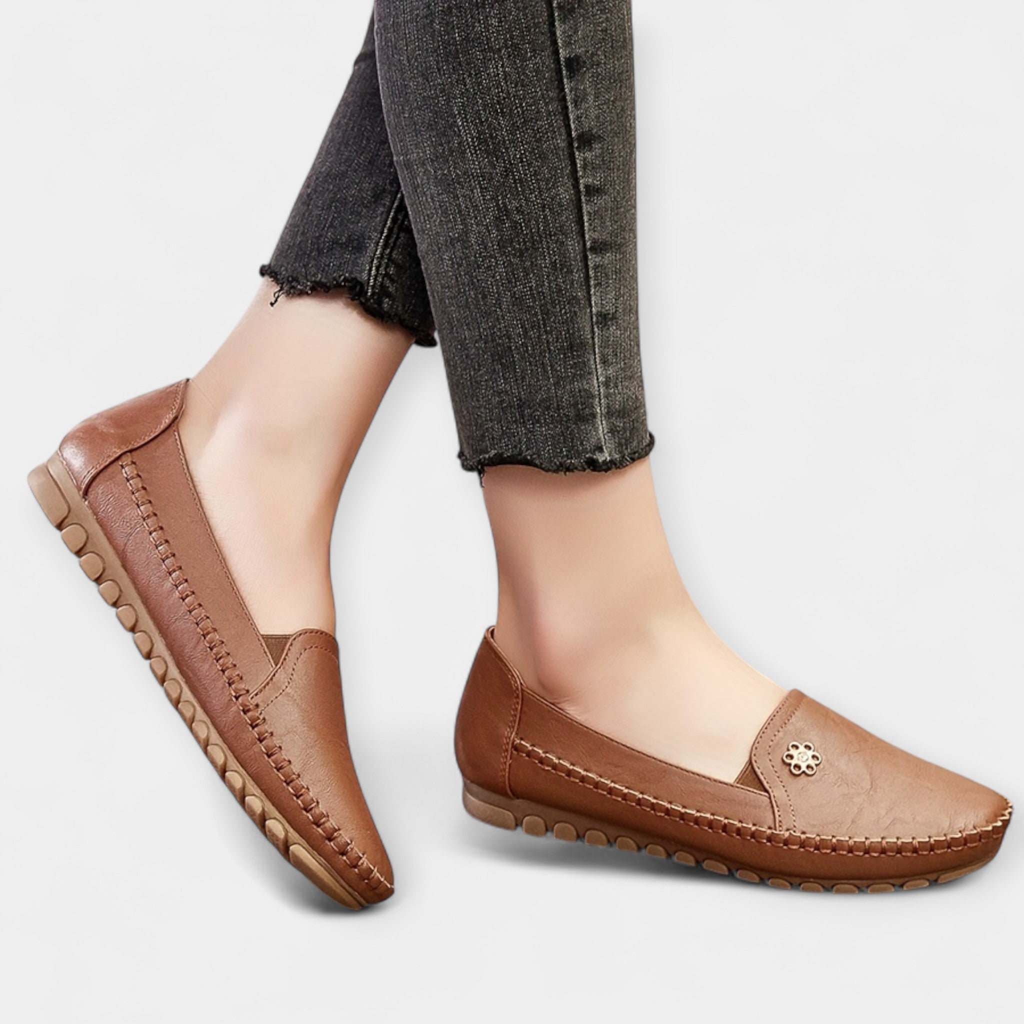 Dark brown slip-on loafers with soft sole, stitched trim, and small floral emblem detail