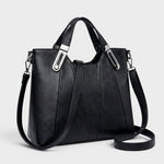 Black leather handbag with top handles, metal buckles, and long crossbody strap