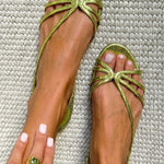 Metallic gold strappy flat sandals with green bow-like accent at toe