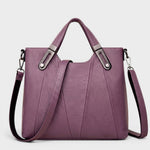 Purple leather handbag with top handles, metal buckles, and detachable side strap