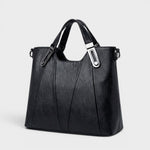 Black leather handbag with top handles, front seam panels, and shoulder strap