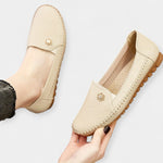 Beige slip-on loafers with soft sole, stitched side seams, and floral emblem on upper