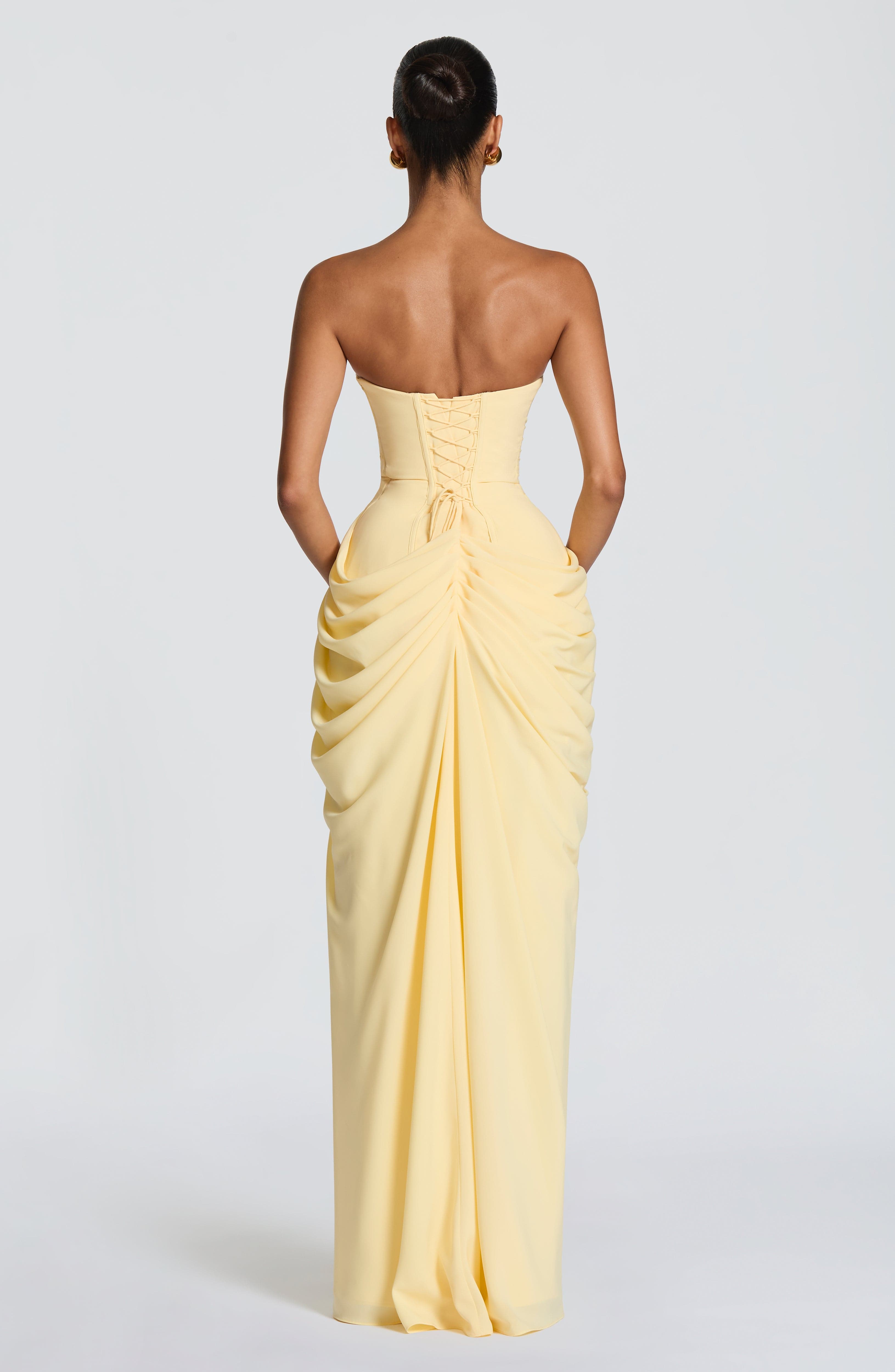 Back view of pale yellow strapless corset maxi dress with gathered drape and slit