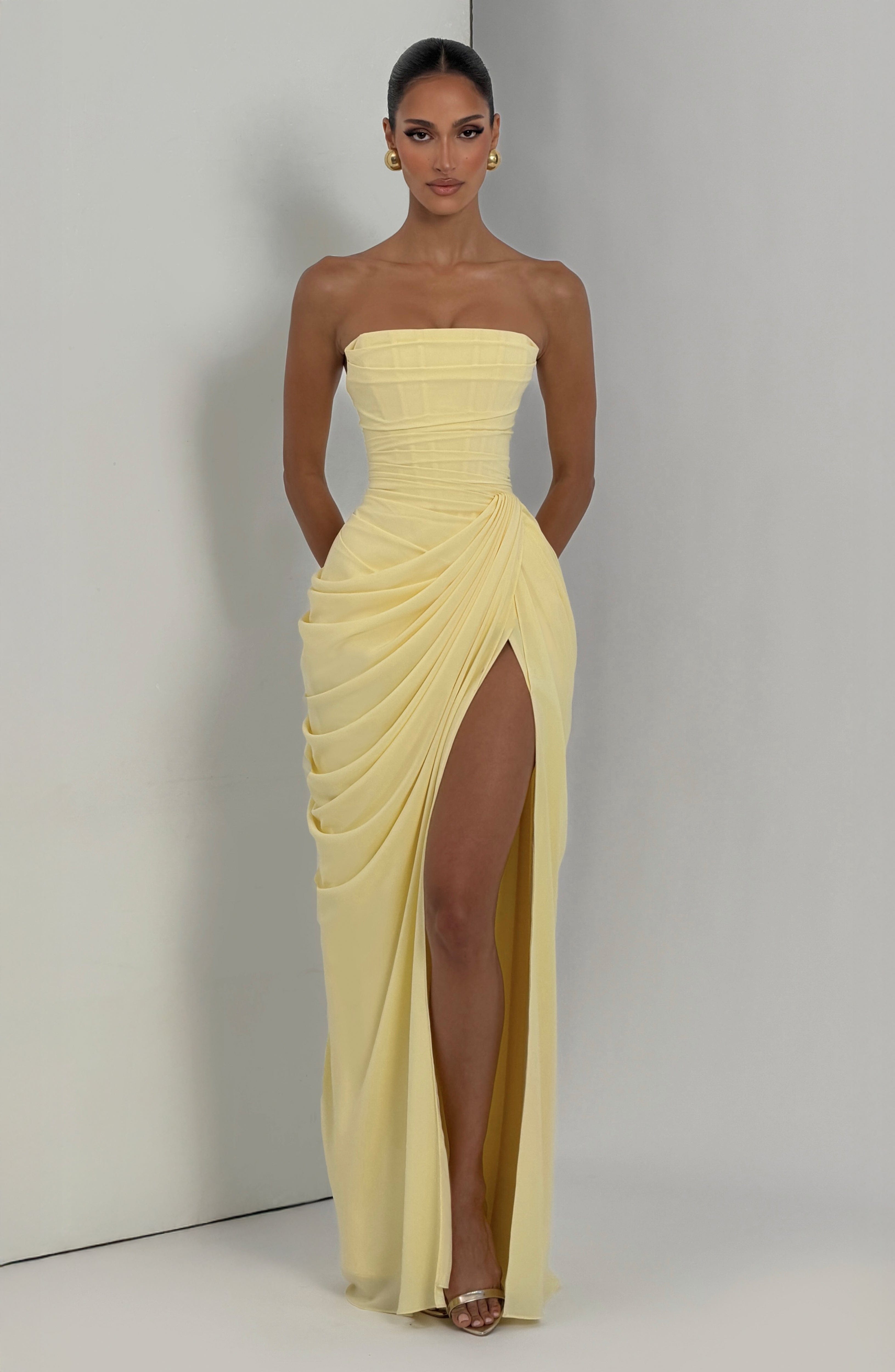Pale yellow strapless corset maxi dress with draped overlay and high front slit