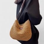 Tan woven crescent shoulder bag with long brown crossbody strap and front patch