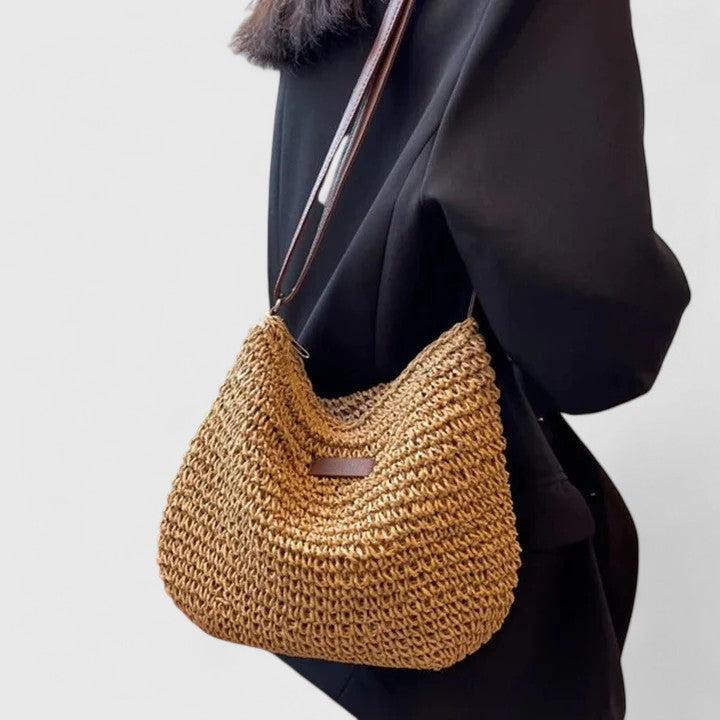 Tan woven crescent shoulder bag with long brown crossbody strap and front patch