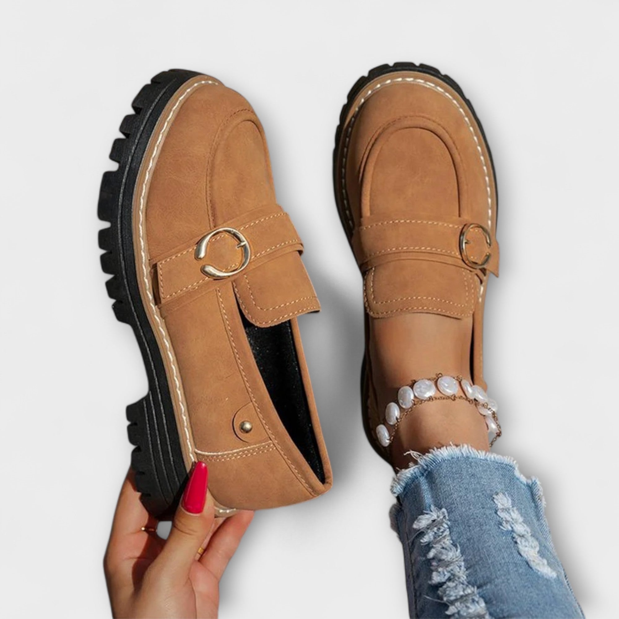 Brown suede moccasin loafers with round toe, metal ring buckle strap, and tread sole