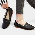 Black slip-on loafers with soft sole, stitched edges, and small floral emblem detail