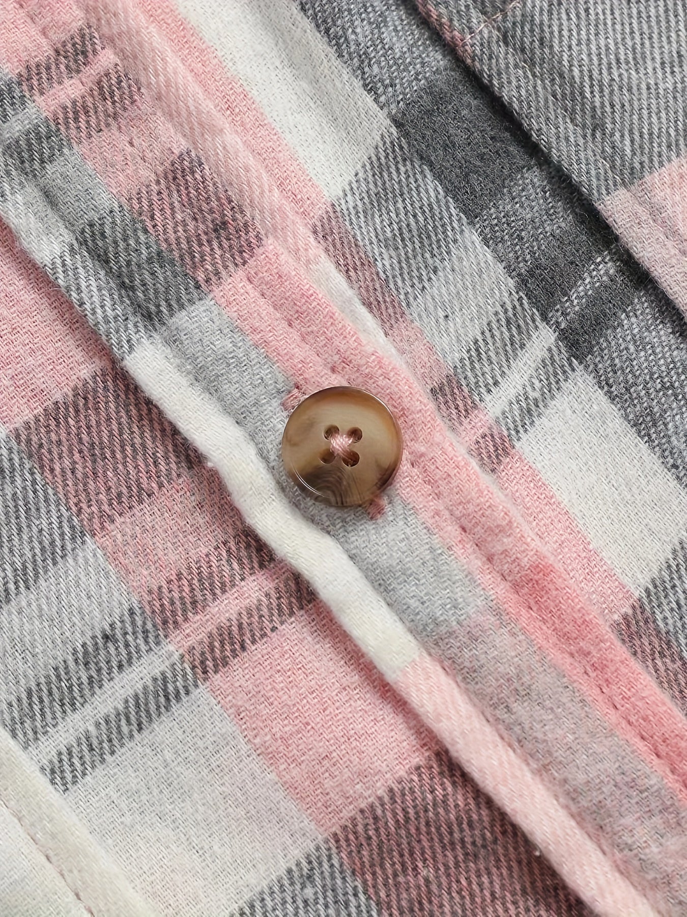 Plaid shirt fabric detail with brown button and white contrast trim
