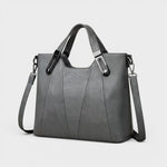 Gray leather handbag with structured sides, top handles, and shoulder strap