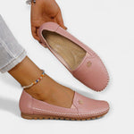 Pink slip-on loafers with soft sole, stitched seams, and small floral emblem on upper