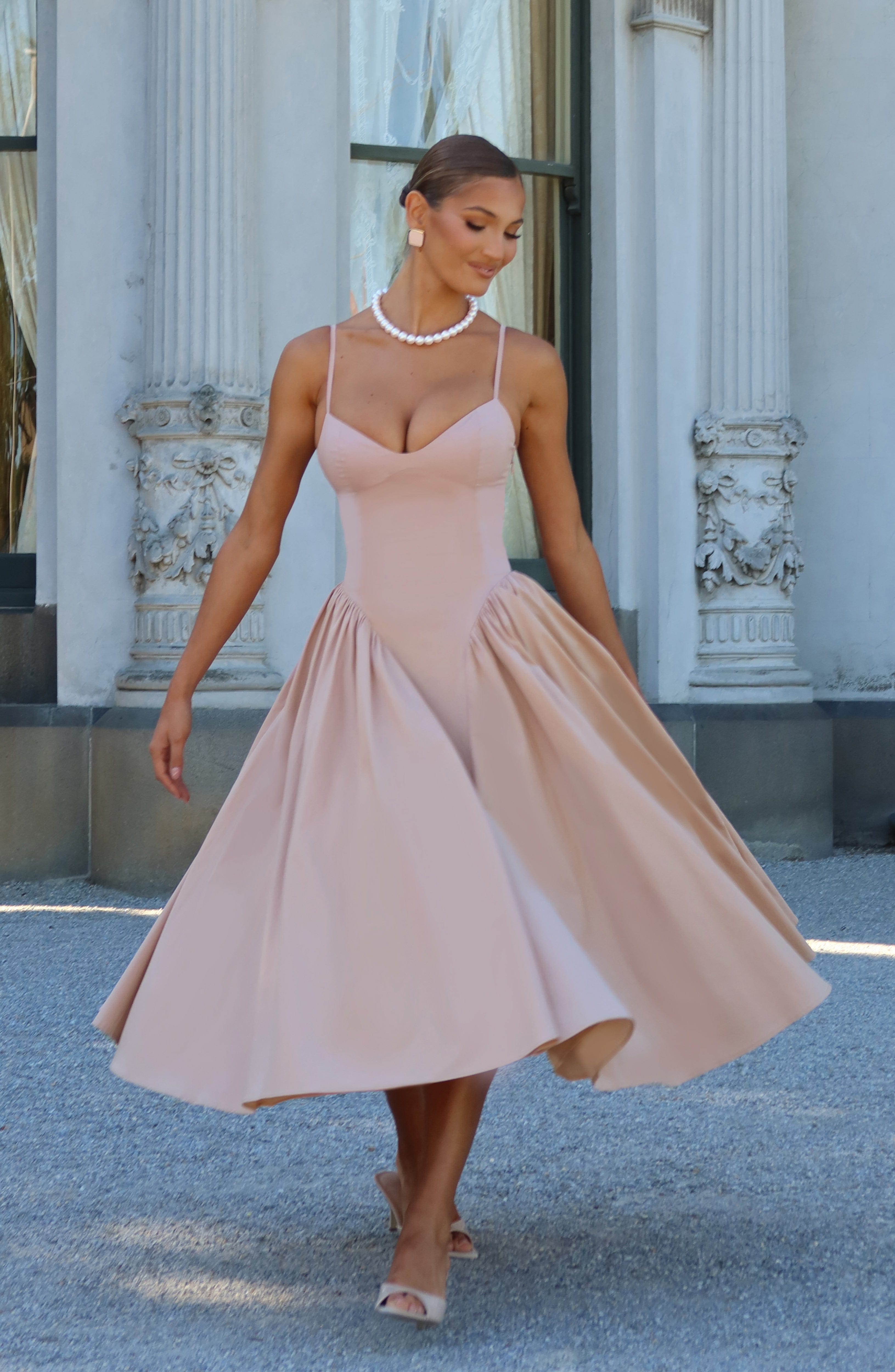Women’s blush midi dress with thin straps and full flared skirt, walking view