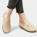 Pair of beige slip-on loafers with floral emblem, stitched details, and brown rubber sole