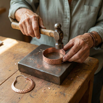 Copper wire hoop earring on a workshop table with metal tools nearby