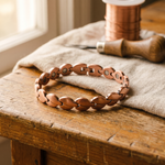 Copper link bracelet with oval cutout plates, laid on a cloth over wood