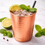 Hammered copper drinking cup with ice, mint leaves, lemon slice, and metal straw