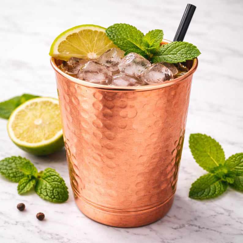 Hammered copper drinking cup with ice, mint leaves, lemon slice, and metal straw
