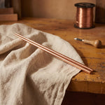 Hammered copper utensil pair with tapered ends, laid on cloth.