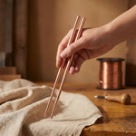Hammered copper utensil pair held in hand, with tapered ends.