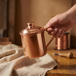 Hand-held hand-beaten copper jug with domed lid and side handle, polished finish