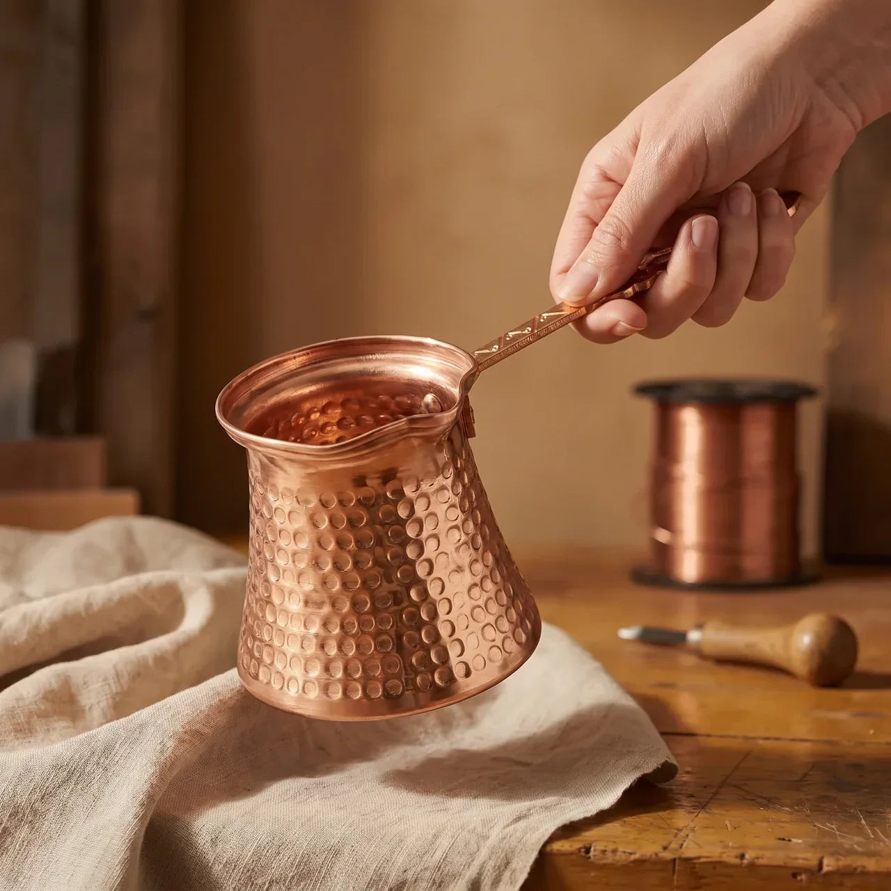 Hammered copper Turkish coffee pot held by hand, open top