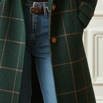 Dark green plaid tweed coat hem with front buttons over blue jeans