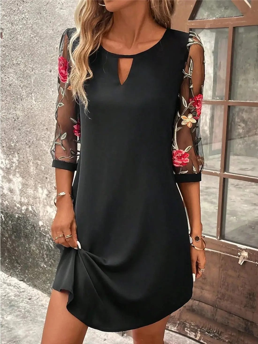 Black shift dress with cutout neckline, sheer floral sleeves, and draped hem
