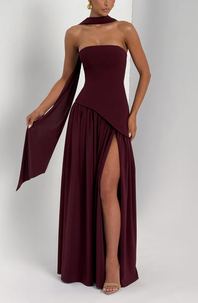 Front view of burgundy strapless maxi dress with draped side panels and leg slit