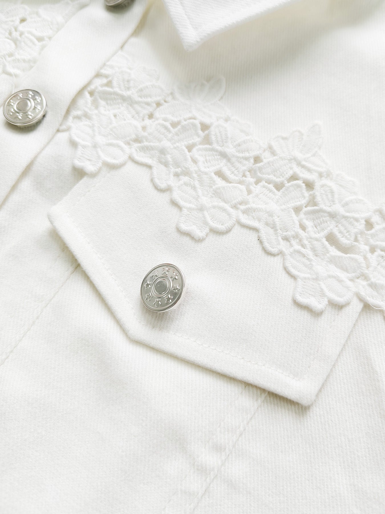 White jacket close-up with silver buttons and embroidered lace yoke