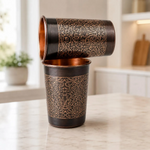Two copper mugs, one showing copper interior; dark bronze exterior with gold floral design