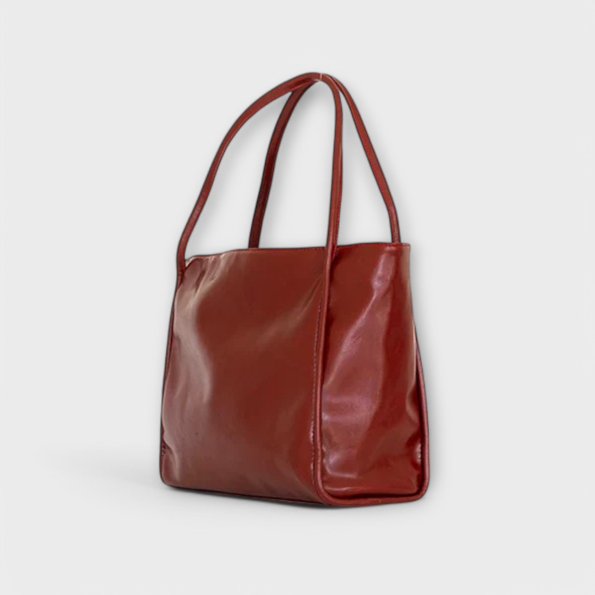 Red leather-look tote bag, side view with double handles and stitched edges
