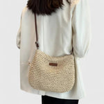 Beige woven crescent shoulder bag with brown leather strap and front metal bar