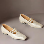 Cream Mary Jane flats with double-strap design, brogue perforations, gold buckles