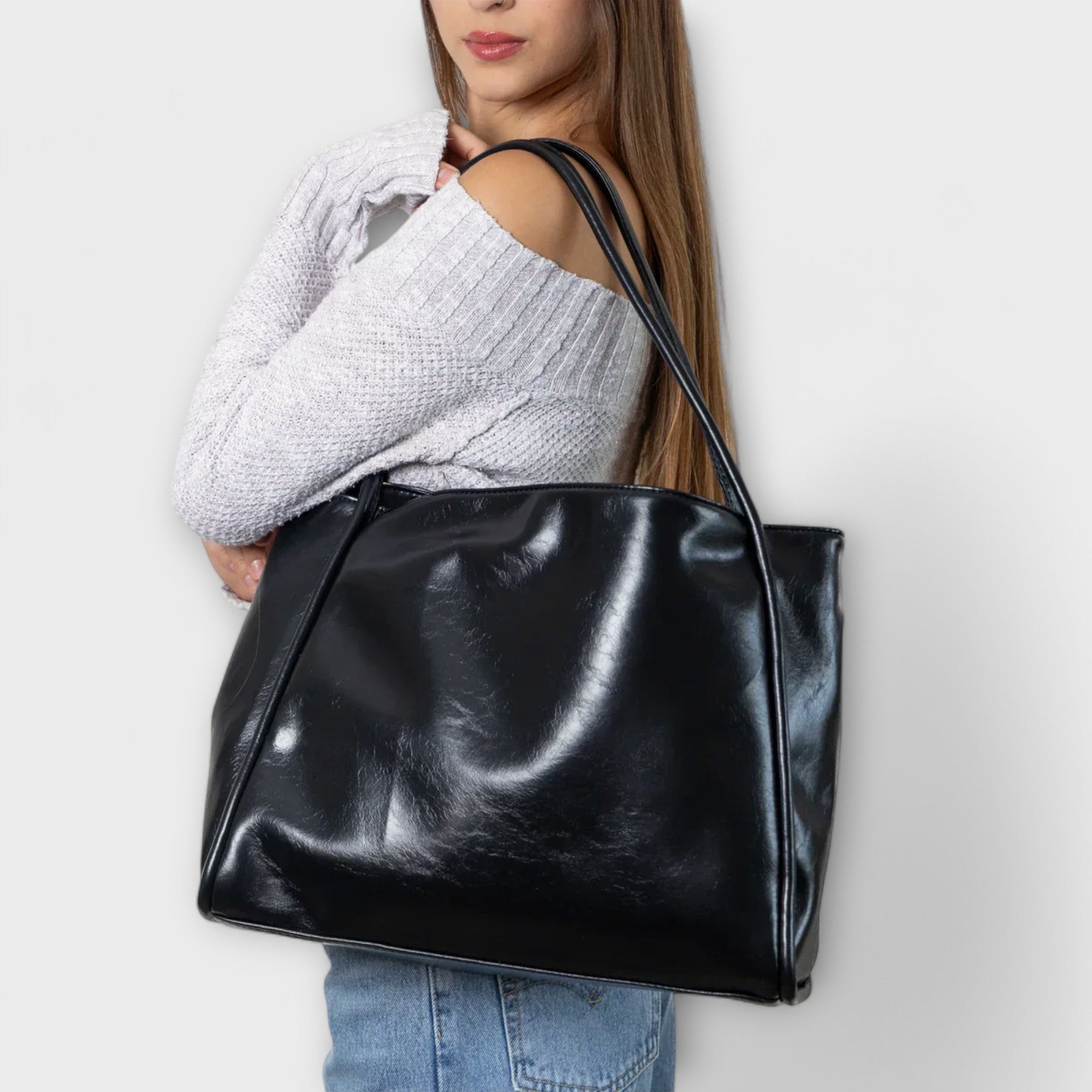 Black leather-look tote bag held by model, wide top opening and stitched seams