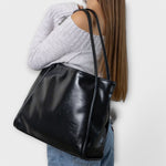 Black leather-look tote bag on model, side view with two top handles