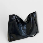 Black leather-look tote bag, angled view with curved double handles